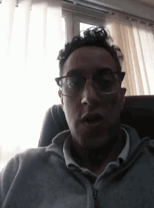 a man wearing glasses and a grey jacket is sitting in front of a window