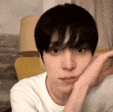 a young man with black hair is sitting in a chair with his hand on his face .