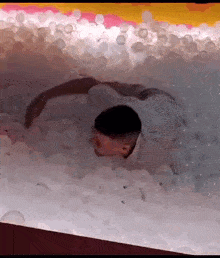 a man is crawling through a ball pit with his head sticking out of it .