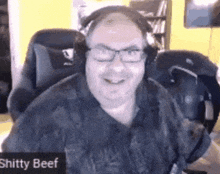 a man wearing headphones and glasses is sitting in a chair with a sign that says shitty beef on it .