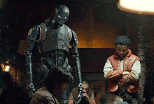 a man in a red vest is standing next to a robot with the letter k on it