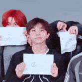 a boy with red hair is holding a piece of paper with the number 2 on it .