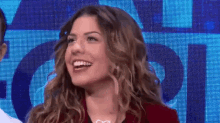 a woman with long curly hair is smiling in front of a blue background .
