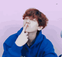a person with red hair is wearing a blue hoodie and covering their mouth with their finger