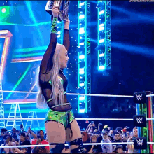 a woman in a wrestling ring is holding a trophy in the air ..