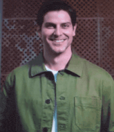 a man in a green jacket is smiling in front of a wall