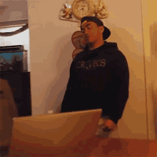a man wearing a hoodie that says crooks is standing in front of a laptop