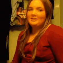 a woman in a red shirt is sitting in front of a wall with clothes hanging on it