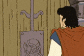 a man in a red cape is standing in front of a wooden door with a drawing on it .