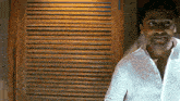 a man wearing a white shirt stands in front of a wooden door