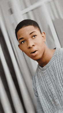 a young man wearing a grey sweater looks surprised at the camera