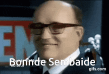 a bald man wearing glasses and a suit says bonnde sembaide