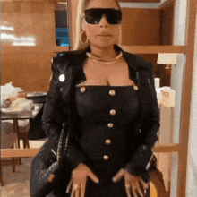 a woman wearing sunglasses and a black dress is standing in a room .