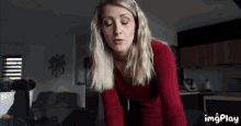 a woman in a red sweater is looking at the camera with imgplay written on the bottom right