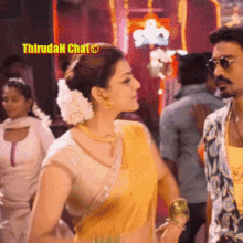 a woman in a yellow saree is standing next to a man in sunglasses in a crowded room .