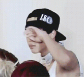a man wearing a black hat with the word lko on it is covering his face with his hand .