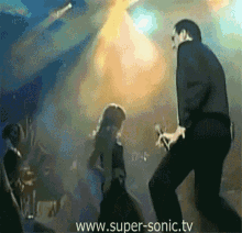 a man singing into a microphone with the website www.super-sonic.tv in the background