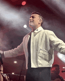 a man in a white jacket is standing on a stage with his arms outstretched