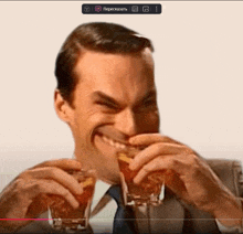 a man in a suit and tie is holding two shot glasses and making a face