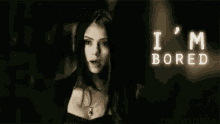 a woman is standing in a dark room with the words `` i 'm bored '' written in white letters .