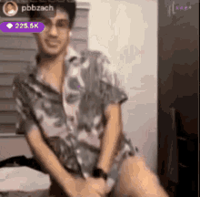 a man in a floral shirt is sitting on a bed with his legs crossed and a purple heart icon in the corner