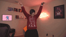 a man in a red sweater is dancing in a room with a neon sign that says just dance