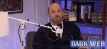 a man sitting in front of a microphone with a sign that says dark web on it