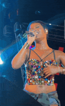 a woman singing into a microphone while wearing a very colorful top