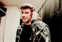 a young man in a plaid shirt is smiling while adjusting his ear .