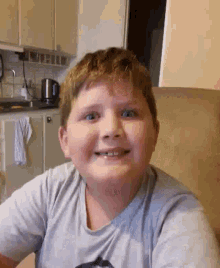 a young boy is smiling and looking at the camera while sitting in a chair .