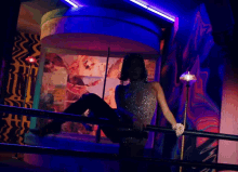 a woman sitting on a railing in a dark room with a blue light behind her