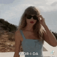 a woman wearing sunglasses and a blue tank top is standing in front of a mountain .