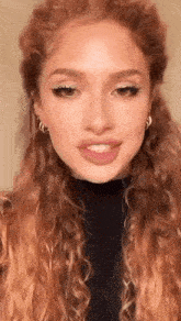 a close up of a woman with curly red hair wearing earrings and a black turtleneck .