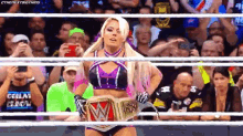 a female wrestler is standing in a ring holding a wrestling championship belt .