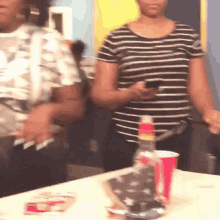 a woman in a striped shirt is standing next to a table holding a cell phone