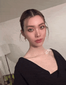 a woman is wearing a black dress and earrings and looking at the camera .