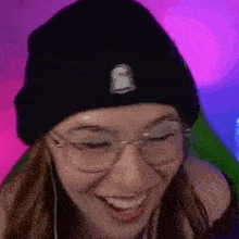 a woman wearing glasses and a black beanie is smiling and laughing .