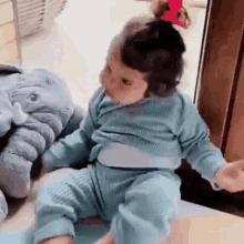 a baby is sitting next to a stuffed elephant and playing with it .
