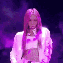 a woman with pink hair is wearing a white jacket and a purple top .