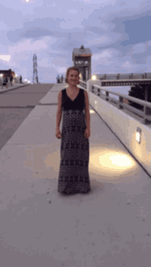 a woman in a long dress stands on a walkway