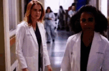 two female doctors are walking down a hallway in a hospital .