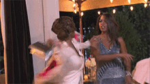 two women are having a fight while standing next to each other in a room .
