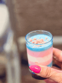 a woman with pink nails is holding a shot glass filled with blue and pink candy