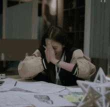 a woman is sitting at a table with her hands folded in front of her face