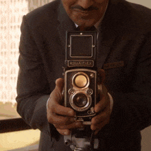 a man holds a rolleiflex camera in his hands