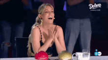 a woman is laughing while sitting at a table in front of a deluxe logo