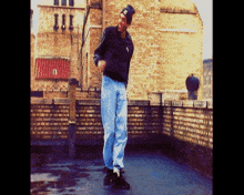 a man wearing a black jacket and a black beanie is standing on a rooftop