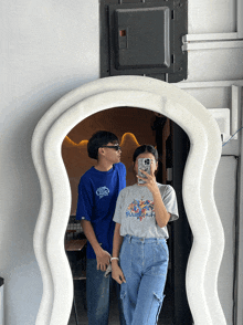 a couple taking a picture in front of a large mirror