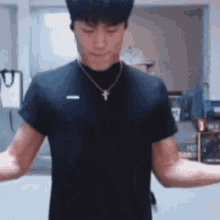 a man wearing a black t-shirt and a cross necklace is flexing his muscles in a room .