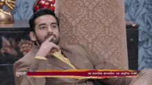 a man in a suit sits on a couch with a red banner above him that says ' shudhna ' on it